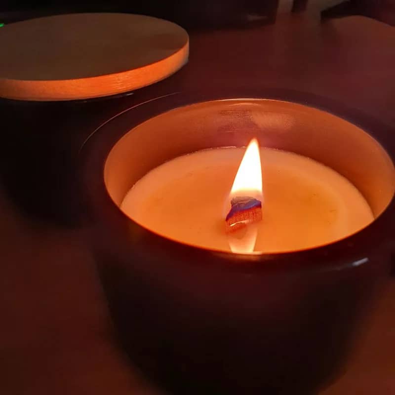 100% soy candle burning in black ceramic container with a wooden wick